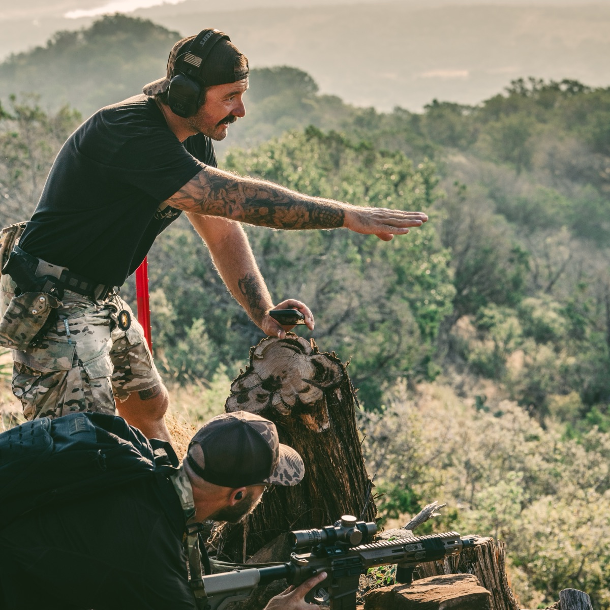 An instructor pointing out a target to a shooter behind the rifle on the mountain